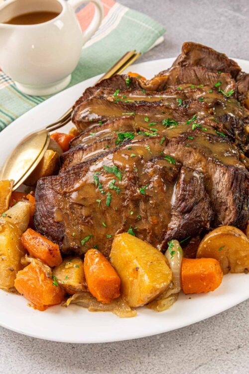 Juicy beef roast with roasted vegetables and gravy on a white platter, perfect for comfort food.