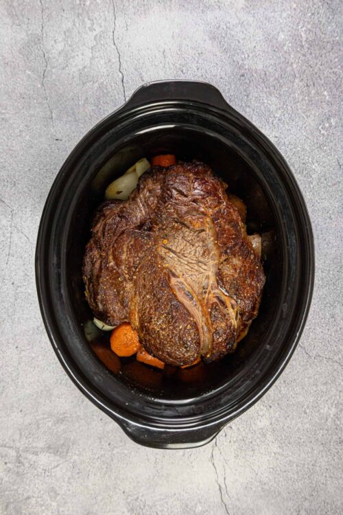 Slow cooker pot roast with vegetables in black crockpot, tender beef and hearty comfort food, easy family dinner recipe.