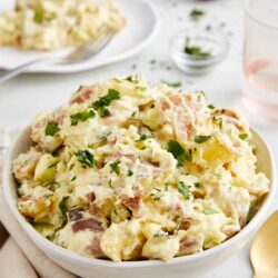 Creamy potato salad with herbs and ham, served in a white bowl. Perfect for picnics and summer gatherings.