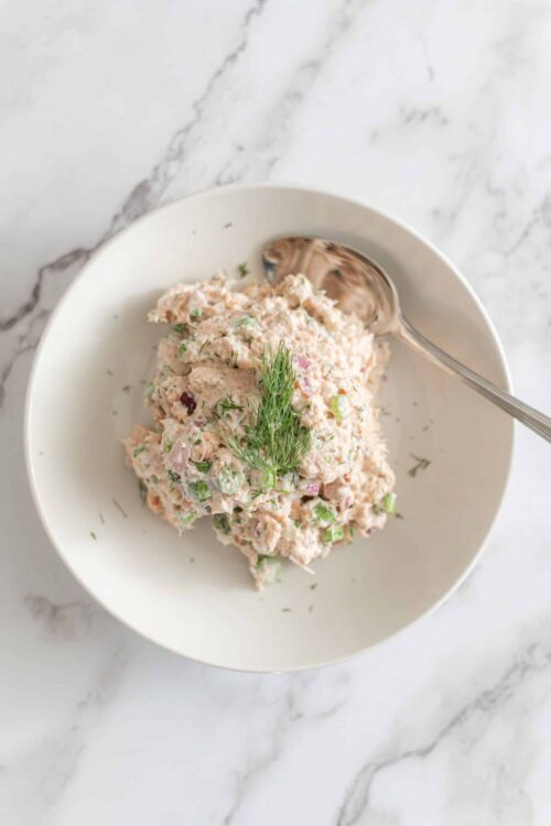 Creamy seafood salad with diced vegetables and fresh herbs on a white plate.