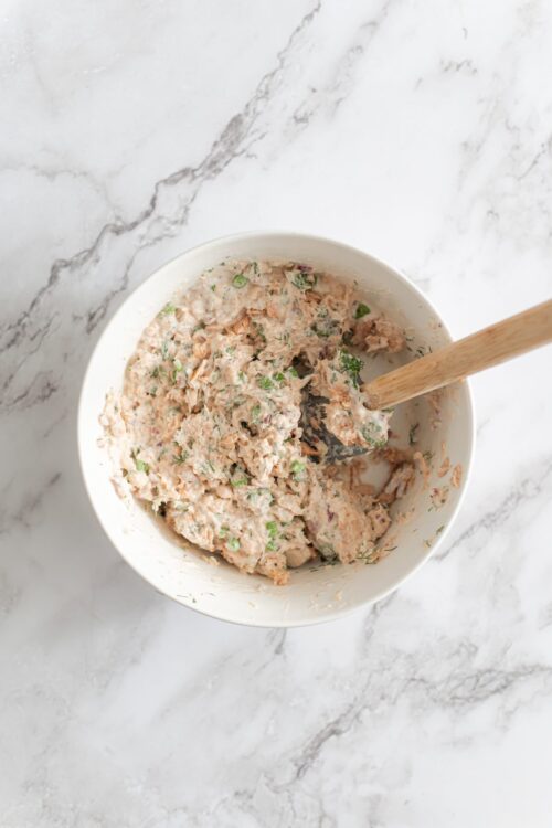 Creamy tuna salad with chopped vegetables in a white bowl on a marble surface.