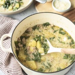 Creamy potato kale soup in a white enamel pot with a ladle, served with toppings in the background.