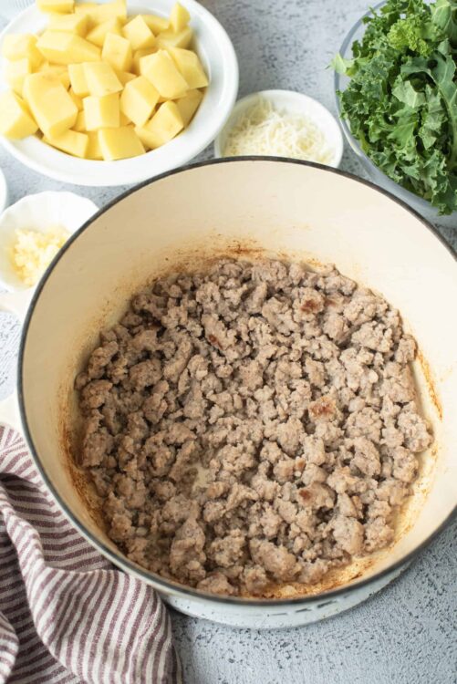 Cooked ground beef in a large pot with ingredients for a savory recipe.