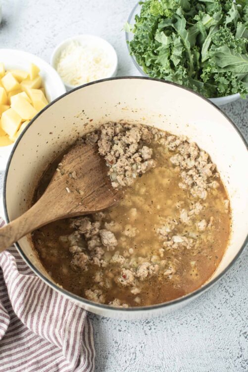 Creamy ground beef and vegetable soup in a large pot with fresh ingredients nearby.