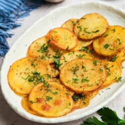 Thinly sliced crispy roasted potatoes garnished with fresh herbs on a white platter.