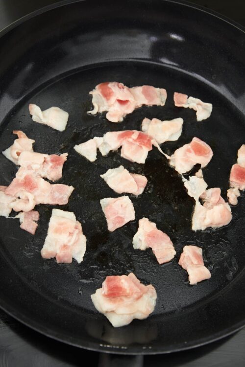 Sizzling bacon cooking in a black skillet, crispy pancetta for breakfast or brunch.