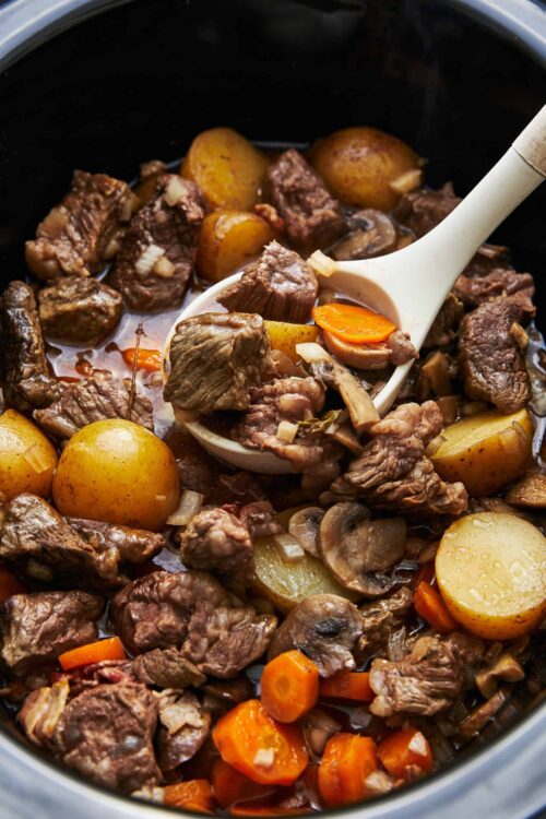 Savory beef stew with potatoes, carrots, and mushrooms cooking in a slow cooker.
