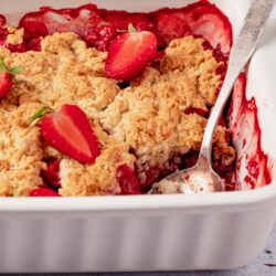 Fresh strawberry crisp with golden topping and ripe strawberries in a white baking dish.