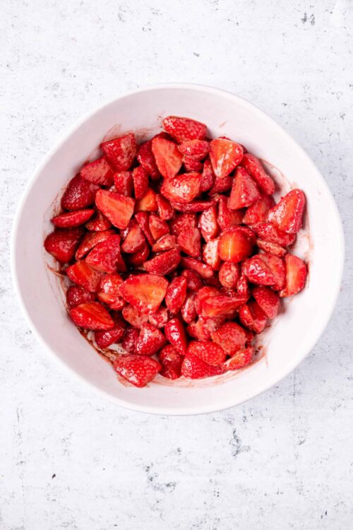 Fresh strawberries cut into pieces in a white bowl for baking or dessert recipes.