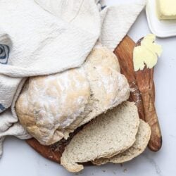 Flour-dusted bread dough on wooden cutting board with butter and baking towel.