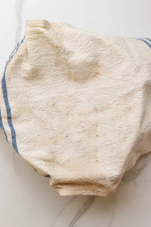 Crumbled linen dish towel on white marble surface, used for baking or kitchen cleanup.