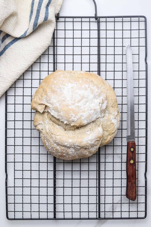 Fresh homemade bread dough on a cooling rack with a bread knife and a kitchen towel.