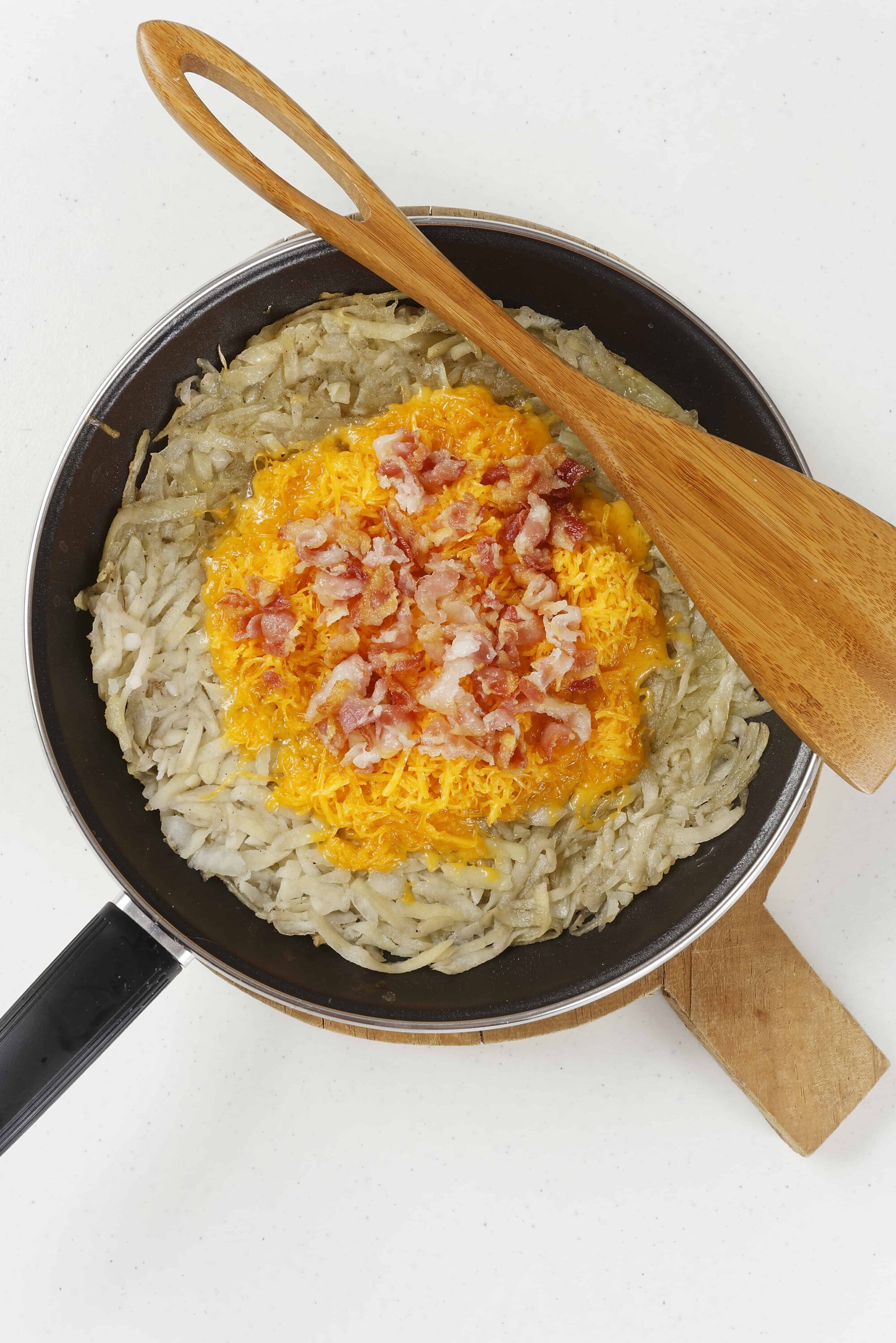 Crispy hash browns with shredded cheese and bacon in a frying pan.