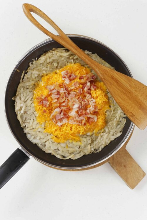 Crispy hash browns with shredded cheese and bacon in a frying pan.