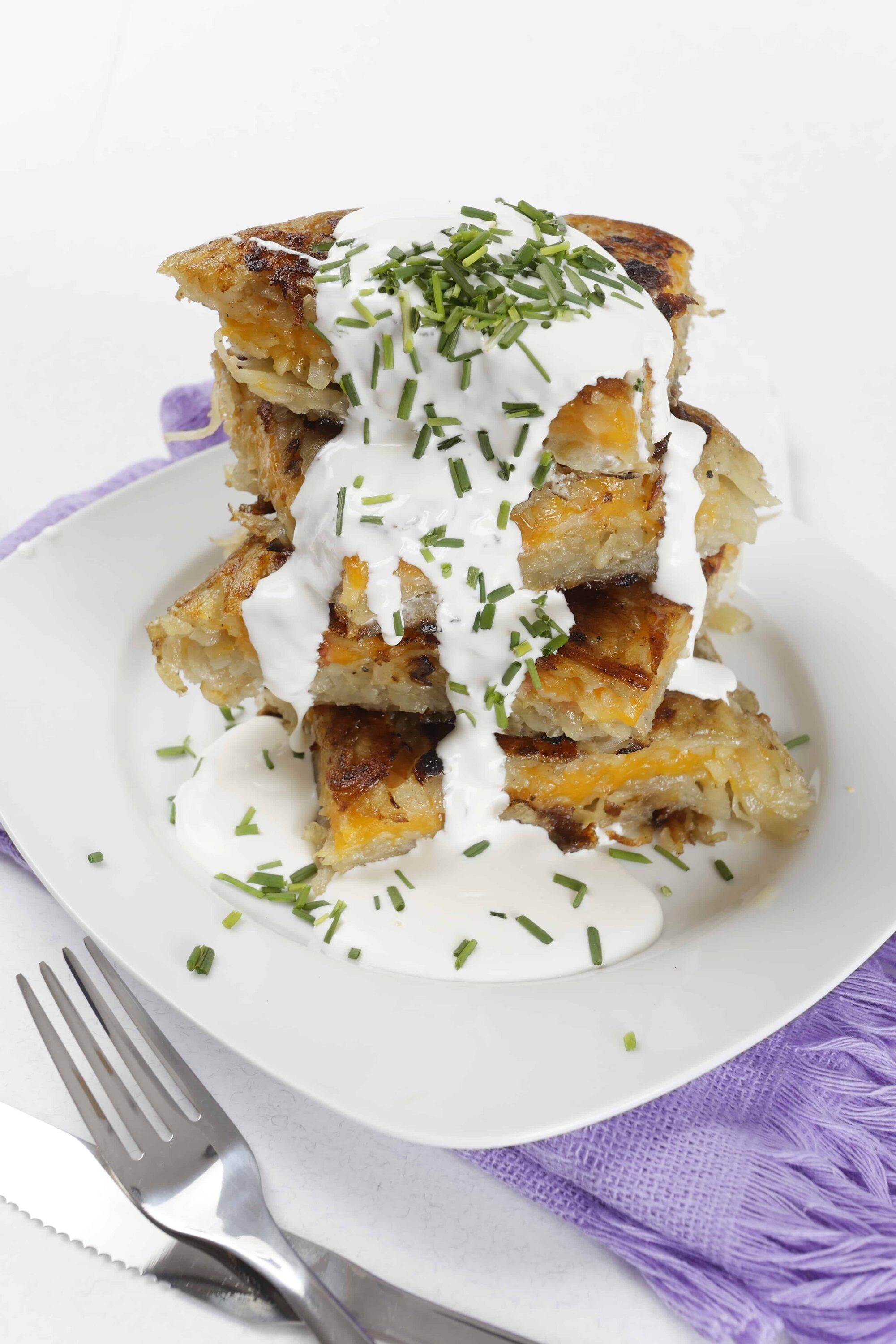 Crispy hash brown casserole topped with sour cream and chives, served on a white plate.