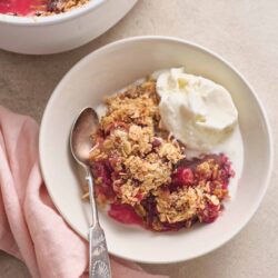 Cherry crumble dessert with vanilla ice cream on a white plate, baked in a white dish.