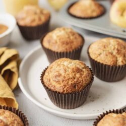 Freshly baked apple cinnamon muffins in paper liners on a white plate.