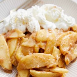 Buttery apple cinnamon crumble with whipped cream on a beige plate.