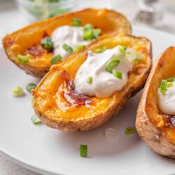 Baked potato halves with cheese, sour cream, and green onions on white plate in close-up.
