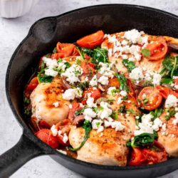 Juicy chicken breast with tomatoes spinach and crumbled feta cheese in cast iron skillet.