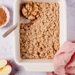 Apple crumble dessert in a white baking dish with fresh apples and crumb topping.