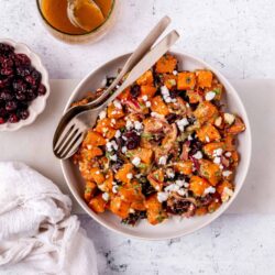 Roasted sweet potato salad with cranberries and feta cheese on white plate.