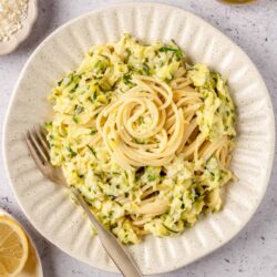 Creamy zucchini and lemon pasta with Parmesan on a white plate, fresh ingredients around, easy vegetarian recipe.