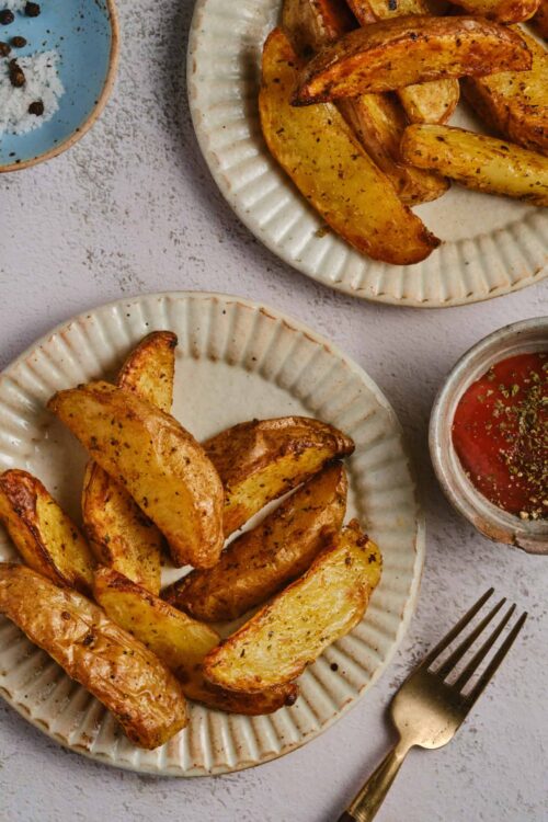 Crispy roasted potato wedges seasoned with herbs on ceramic plates.