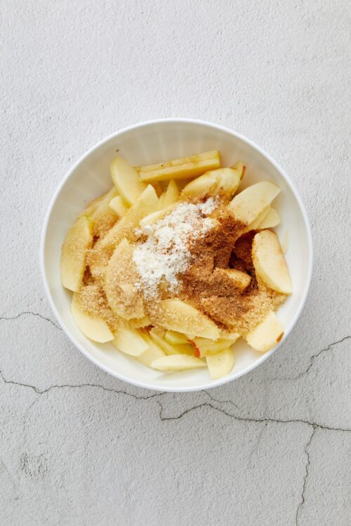 Sweet apple slices with cinnamon and sugar in a white bowl, ready for baking or making apple desserts.