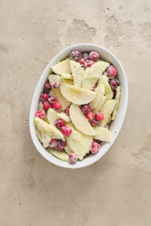 Fresh sliced apples and red cranberries in a white baking dish, ready for a holiday dessert or pie.