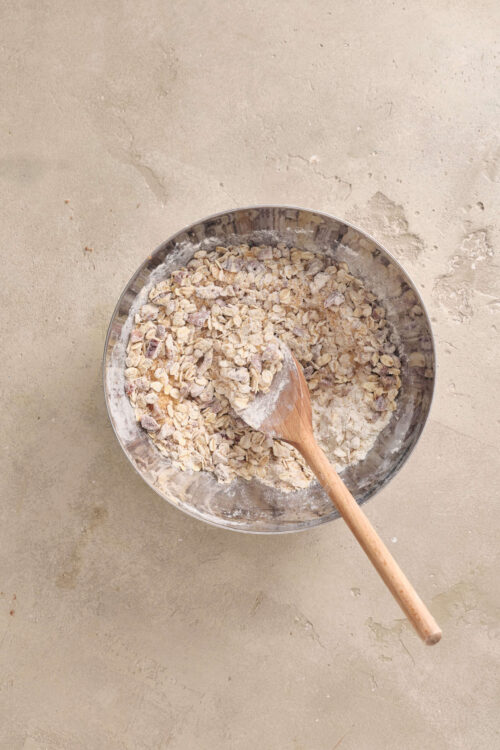 Crushed oats and flour in a mixing bowl for baking, on a neutral background.