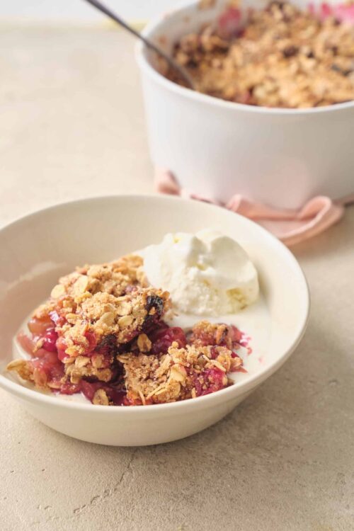 Fresh cherry crisp with oatmeal crumble and vanilla ice cream in a white bowl on a neutral surface.