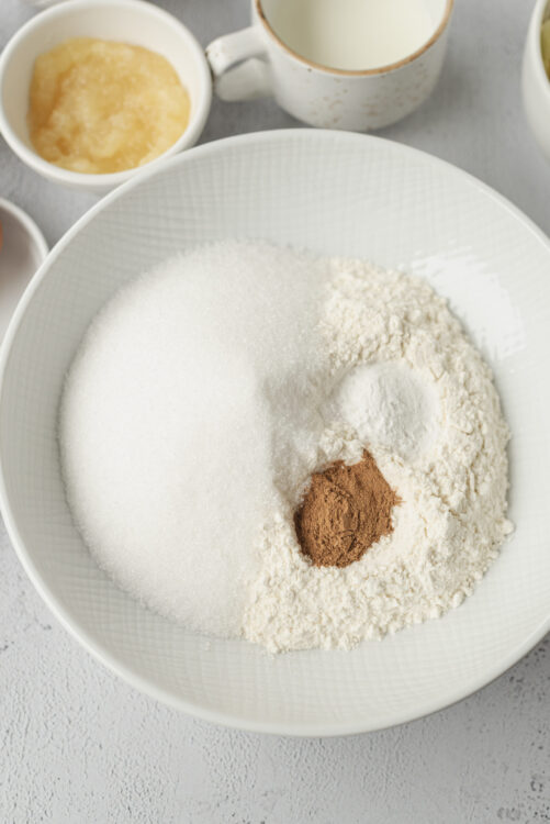 Flour, sugar, cinnamon, and other baking ingredients in a white bowl for baked good recipes.