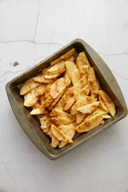 Sliced apples with cinnamon in a metal baking dish for apple dessert or pie.