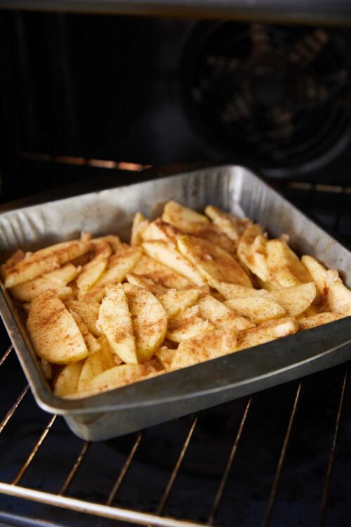 Baked apple slices seasoned with cinnamon in a baking dish in the oven.