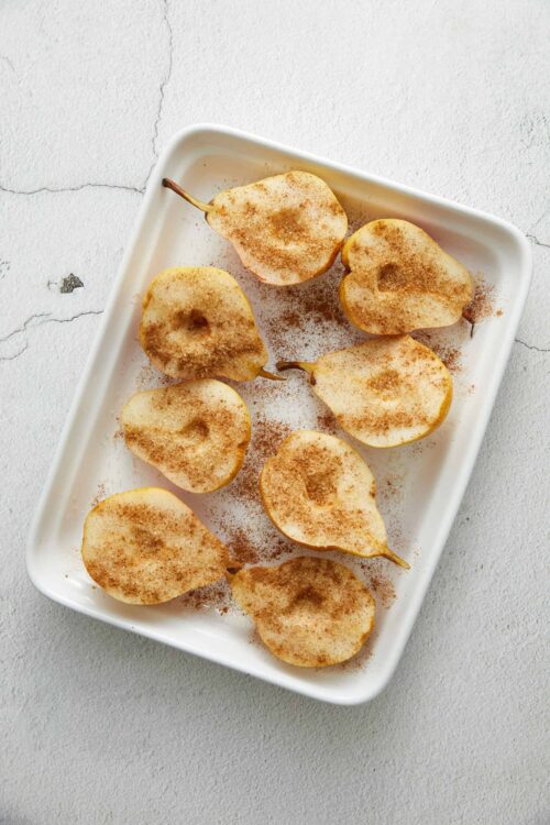 Baked pears sprinkled with cinnamon on a white rectangular dish.