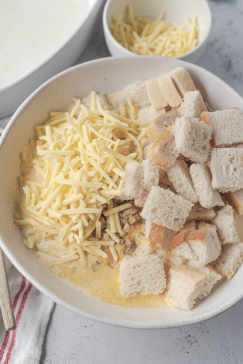 Cream cheese and shredded cheese in a white bowl with bread cubes for cheese fondue.