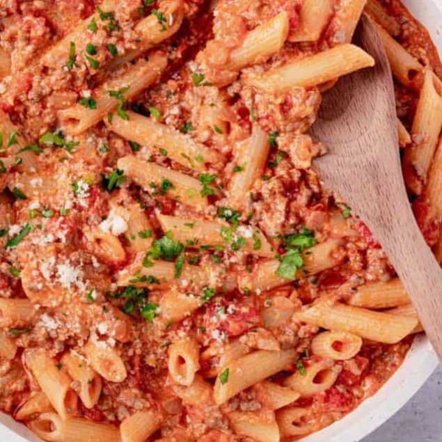 Creamy baked ziti with melted cheese, tomato sauce, and fresh herbs in a white baking dish.