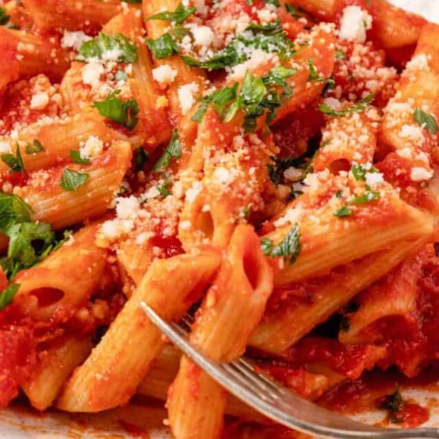 Creamy tomato pasta with fresh herbs and grated cheese, served on a white plate.