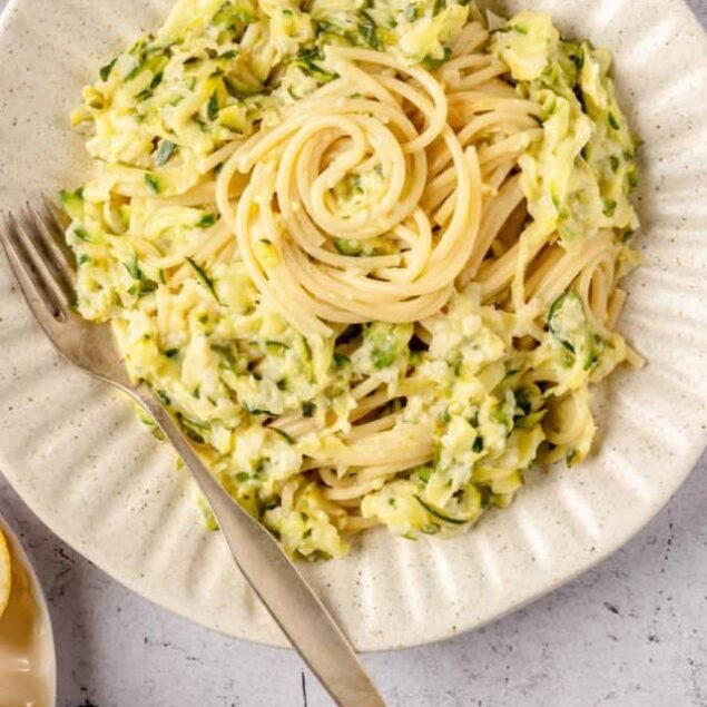 Creamy zucchini and lemon pasta with Parmesan on a white plate, fresh ingredients around, easy vegetarian recipe.