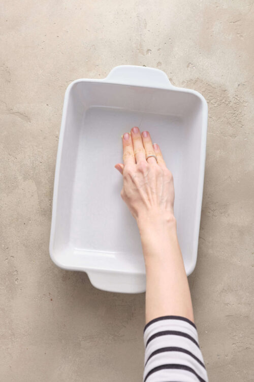 Clean white baking dish with hand smoothing the surface, neutral background, kitchen cookware, baking preparation, culinary tools.