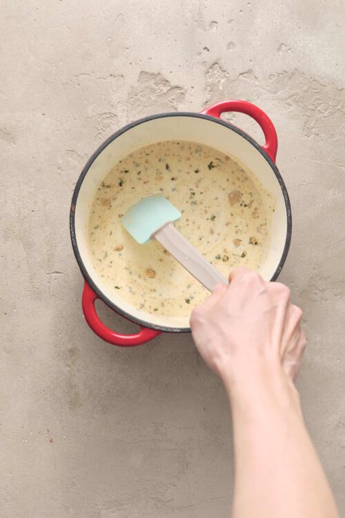 Creamy soup cooking in a red cast iron pot with herbs and spices.