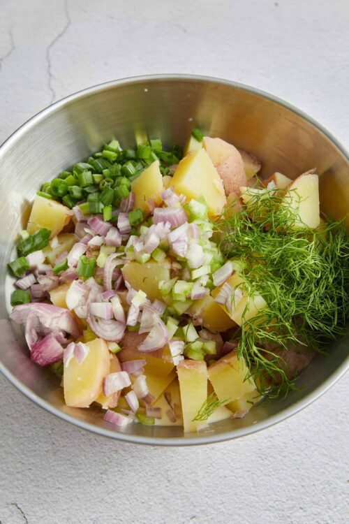 Fresh chopped potatoes, red onions, green onions, and dill in a metal bowl for potato salad.