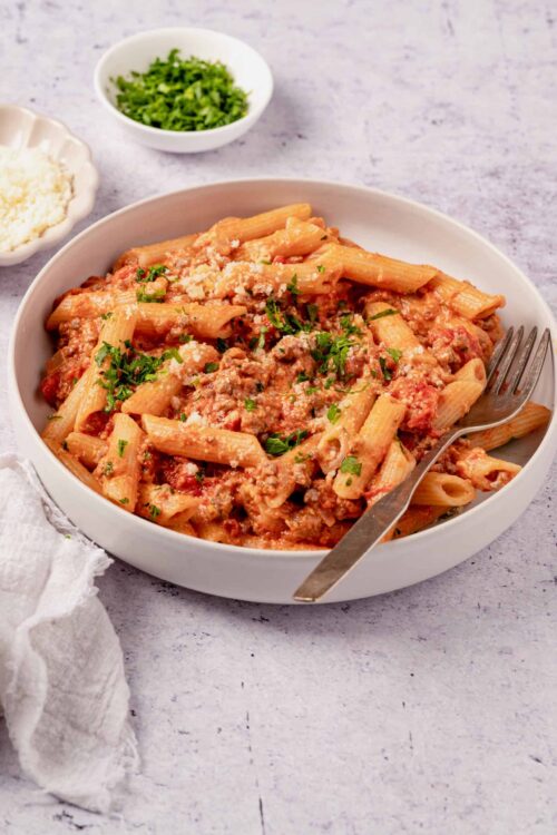 Creamy baked ziti with ground beef, tomato sauce, and melted cheese served in a white bowl.