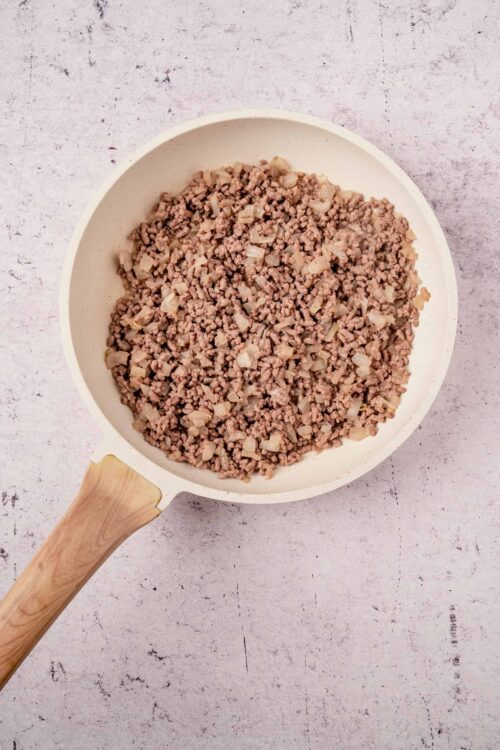 Ground beef and chopped onions in a white skillet.