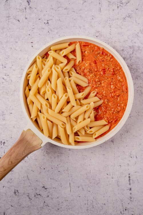 Creamy tomato pasta with penne and ground meat in a white bowl on a textured surface.