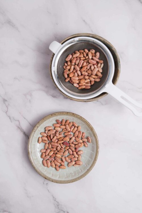 Roasted pinto beans in a sieve and on a plate for baking recipe preparation.