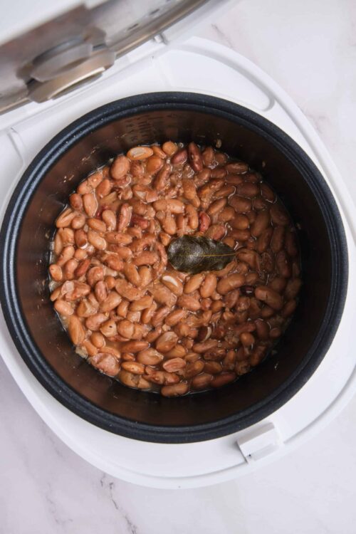 Cooked pinto beans in a slow cooker with a bay leaf.