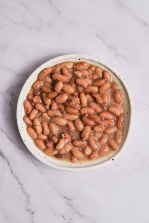 Baked Bree baked beans in a white ceramic dish on a marble surface.