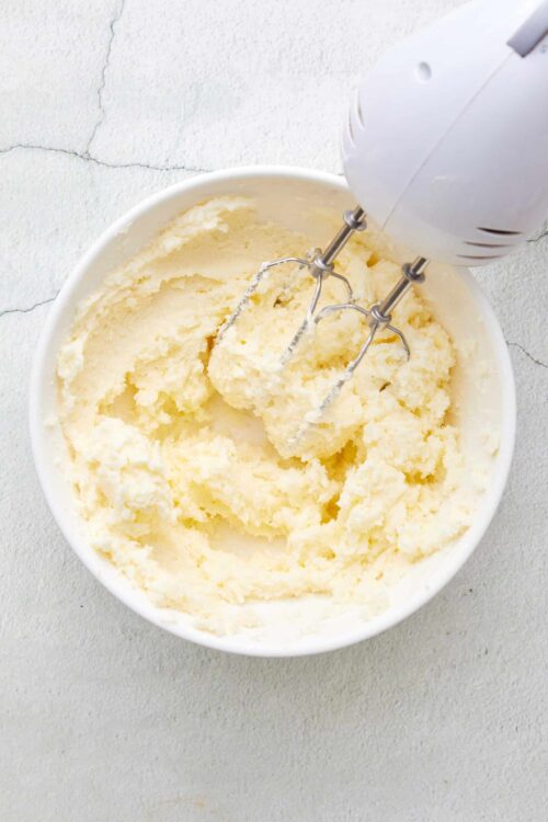 Creamy homemade mashed potatoes with a hand mixer in a white bowl.